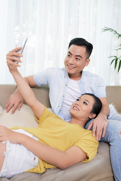 Pareja étnica moderna tomando selfie en sofá