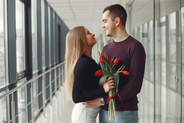 Pareja europea está de pie en una sala con un ramo de tulipanes rojos