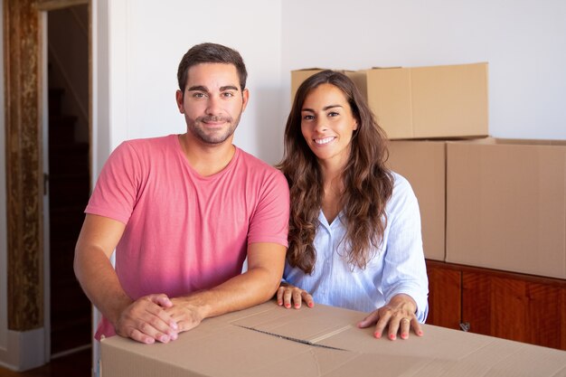 Pareja de familia joven alegre mudarse a casa nueva, de pie en caja de cartón,