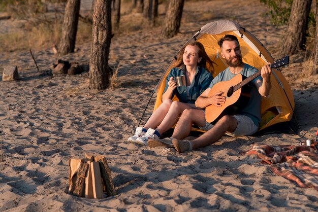 Pareja feliz acampando y tocando la guitarra.