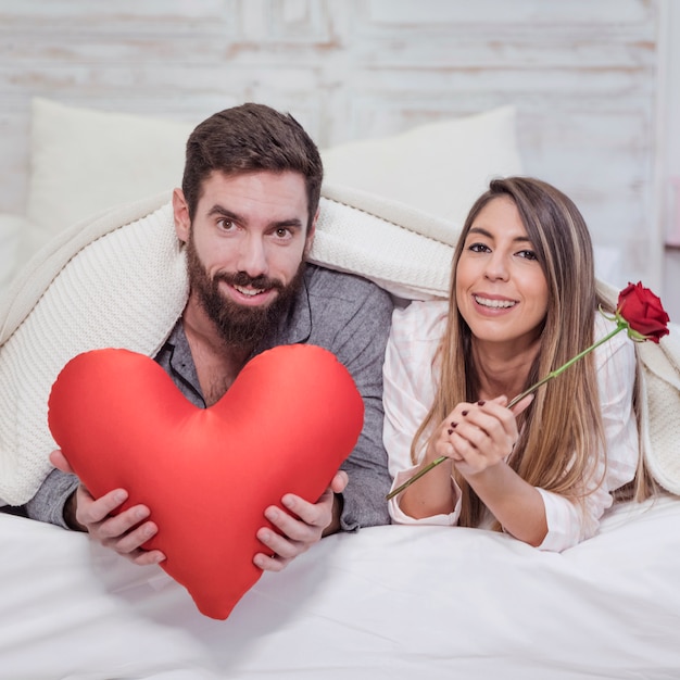 Pareja feliz acostado en cama con corazón rojo suave