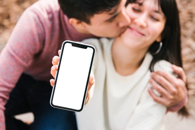 Pareja feliz acurrucándose mostrando teléfono inteligente