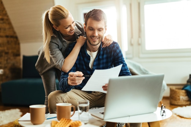 Pareja feliz analizando su presupuesto doméstico mientras paga la factura en una computadora.