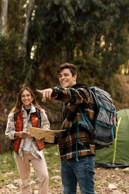 Pareja feliz en el bosque sosteniendo mapa y apuntando