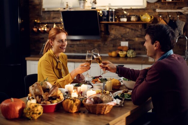 Pareja feliz brindando durante la cena de Acción de Gracias en la mesa de comedor