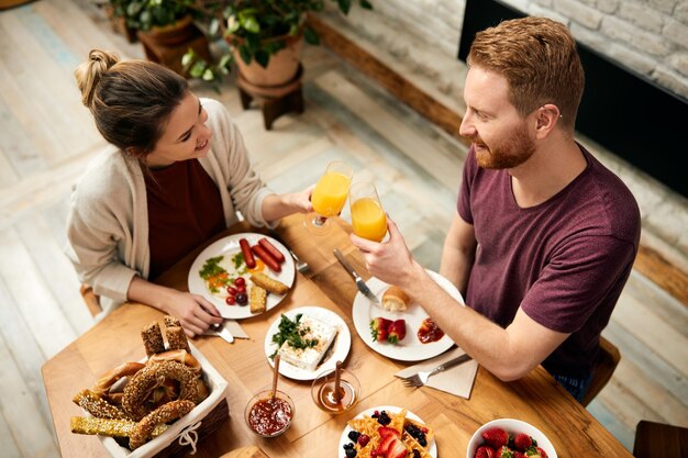 Pareja feliz brindando con jugo de naranja durante el desayuno en casa