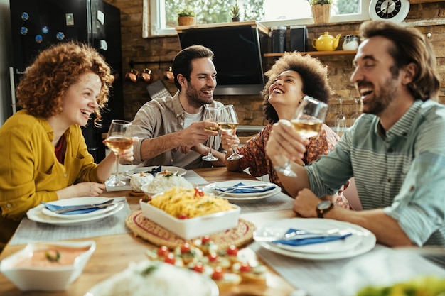 Pareja feliz brindando con vino y divirtiéndose con sus amigos en la mesa de comedor