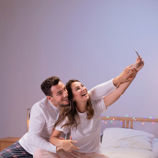 Pareja feliz en la cama tomando selfie