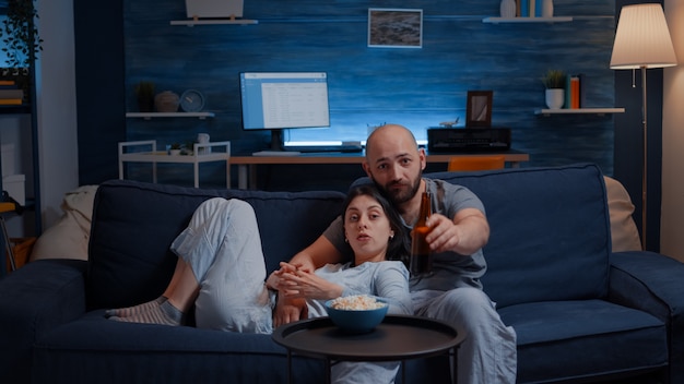 Pareja feliz en casa relajándose en el sofá viendo programas de televisión favoritos