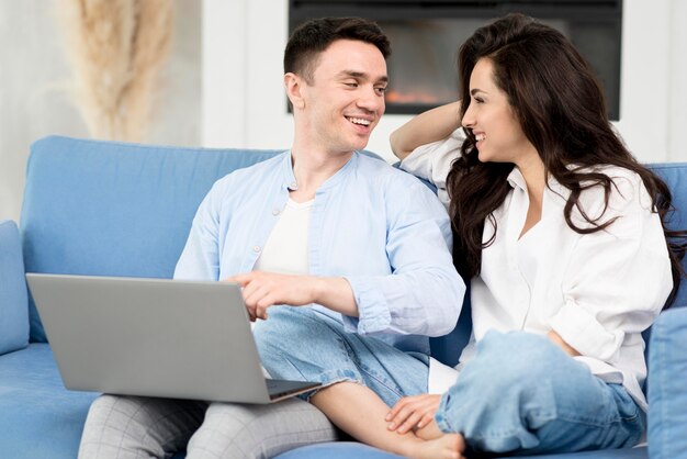 Pareja feliz en casa en el sofá con el portátil