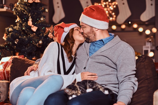 Una pareja feliz celebrando la Nochebuena en casa besándose mientras se sienta en el sofá. Navidad.