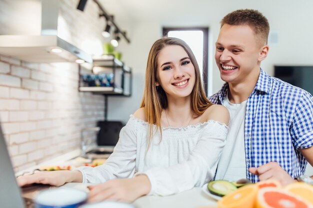 Pareja feliz .. Chica mira la receta en la computadora portátil en casa mientras hace la cena.