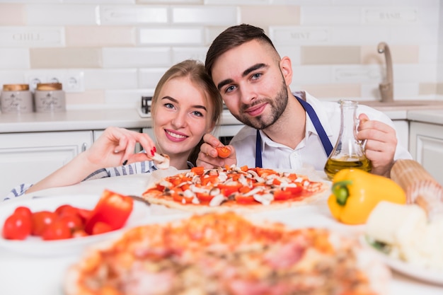 Pareja feliz cocinando pizza con tomates y champiñones en la cocina