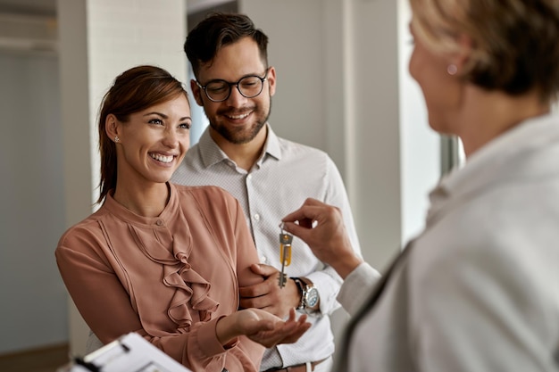 Pareja feliz comprando su nuevo hogar y recibiendo llaves del agente inmobiliario