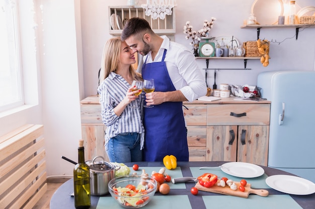 Pareja feliz con copas de vino abrazando en cocina