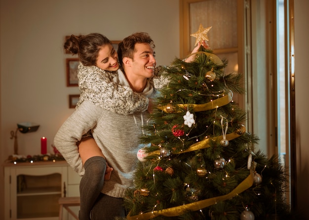 Pareja feliz decorando el árbol de navidad con estrella