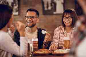 Foto gratuita una pareja feliz disfrutando con amigos mientras bebe cerveza y se comunica en una taberna