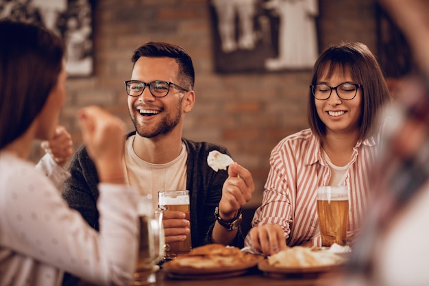 Una pareja feliz disfrutando con amigos mientras bebe cerveza y se comunica en una taberna