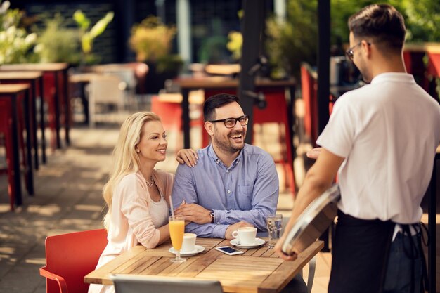 Pareja feliz disfrutando en un café mientras habla con un camarero