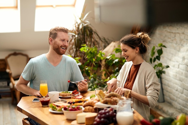 Una pareja feliz disfrutando de una conversación mientras come en la mesa del comedor