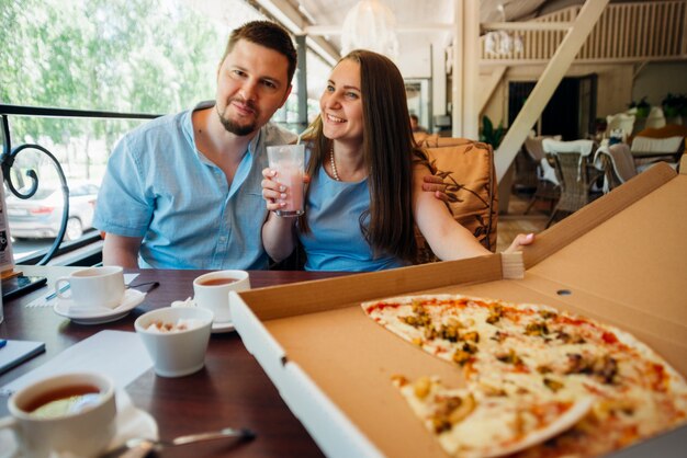 Pareja feliz disfrutando de pizza y batido en café