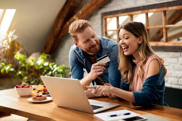 Pareja feliz divirtiéndose mientras compra en línea en casa