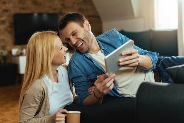 Pareja feliz divirtiéndose y riendo mientras usa el panel táctil en la sala de estar