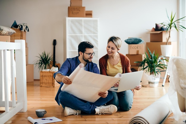 Una pareja feliz examinando planos y usando una laptop en su nuevo apartamento