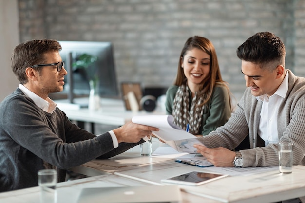 Pareja feliz firmando un contrato en una reunión con su agente inmobiliario en la oficina