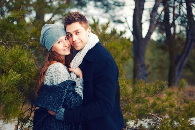 Pareja feliz con gorro y bufanda abrazándose al aire libre en invierno