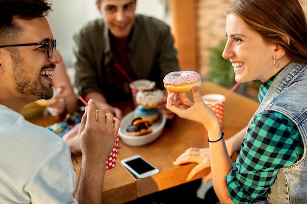 Pareja feliz hablando mientras come donuts con amigos en un café