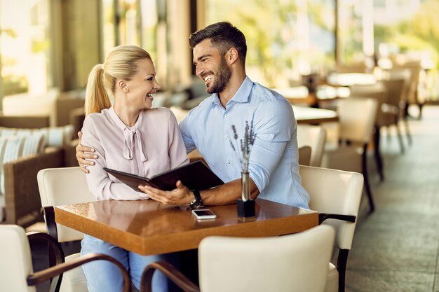 Una pareja feliz hablando mientras elige un pedido de un menú en un café