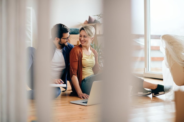 Una pareja feliz hablando mientras usa una laptop en su nuevo departamento