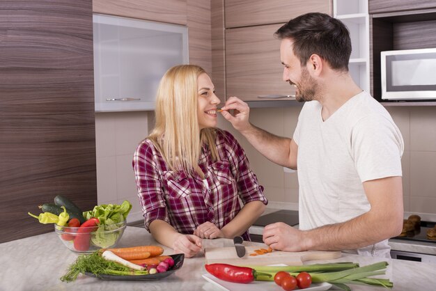 Pareja feliz haciendo una ensalada fresca con verduras en la encimera de la cocina