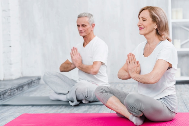 Pareja feliz haciendo meditación en estera de yoga