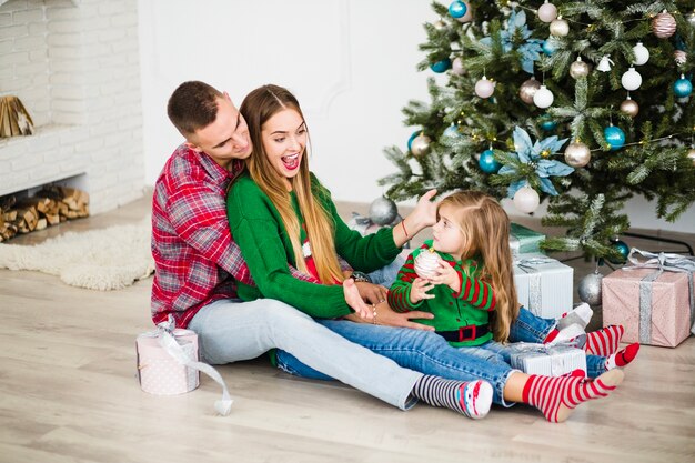 Pareja feliz con hija al lado de árbol de navidad