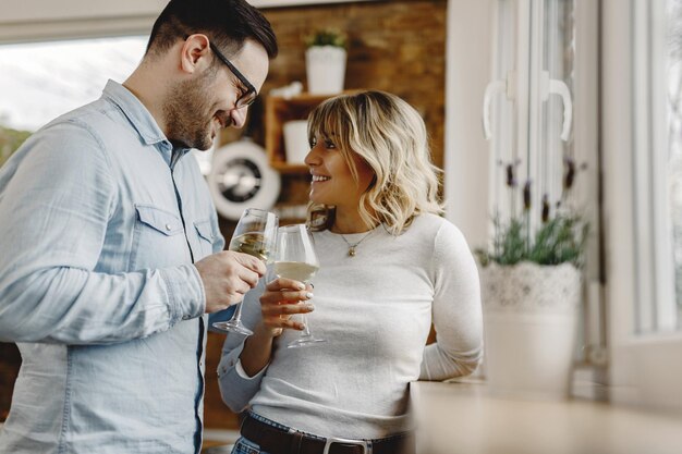 Una pareja feliz mirándose mientras brindan con vino en la cocina