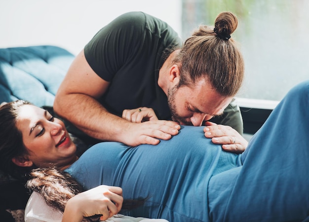 Foto gratuita pareja feliz mujer embarazada y esposo se quedan en casa en la sala de estar pareja feliz cuidando juntos