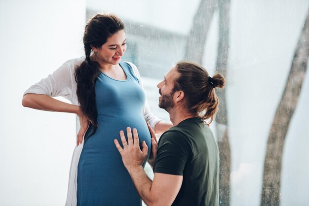 Pareja feliz mujer embarazada y esposo se quedan en casa en la sala de estar Pareja feliz cuidando juntos