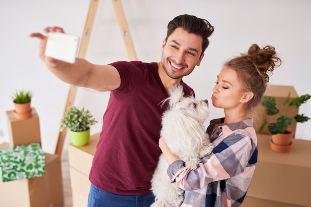 Foto gratuita pareja feliz con perro haciendo un selfie en casa nueva