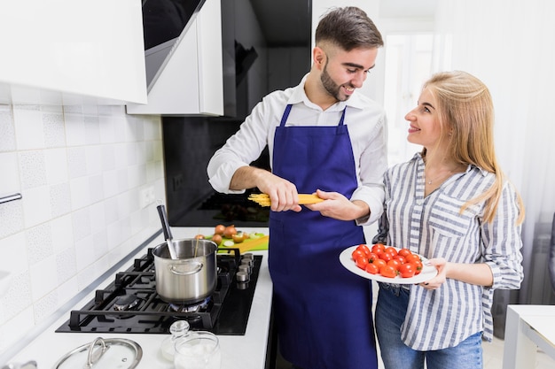 Pareja feliz poniendo espaguetis en una olla con agua hervida