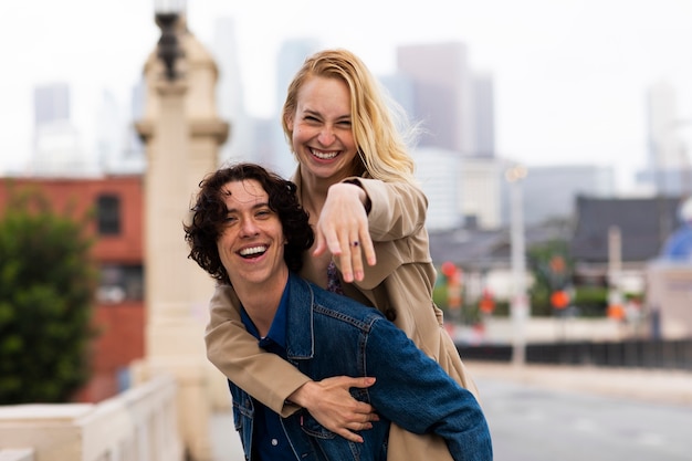 Pareja feliz posando al aire libre en la ciudad con anillo de compromiso