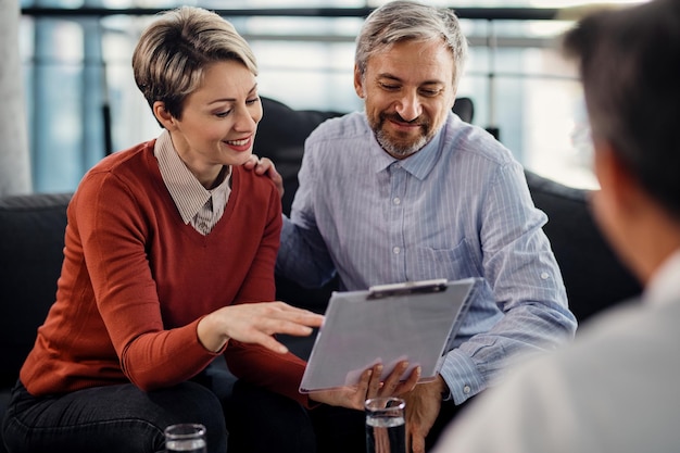 Una pareja feliz revisando los términos de un acuerdo durante una reunión con un asesor financiero