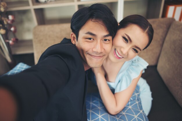 Pareja feliz riendo y tomando un selfie con el teléfono sentado en un sofá en casa