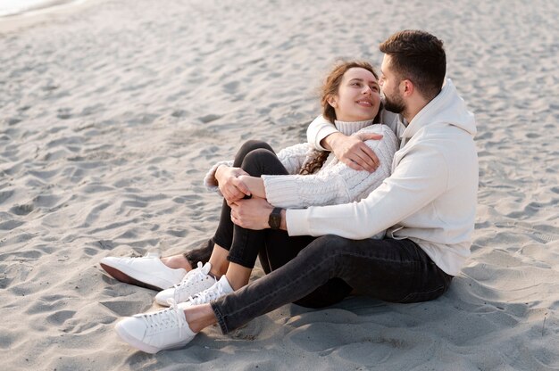 Pareja feliz sentada en la playa tiro completo