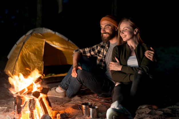 Pareja feliz sentados juntos por la hoguera