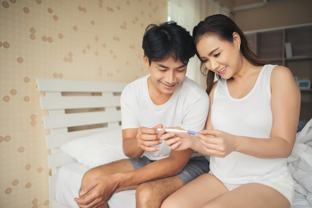 Pareja feliz sonriendo después de descubrir prueba de embarazo positiva en el dormitorio