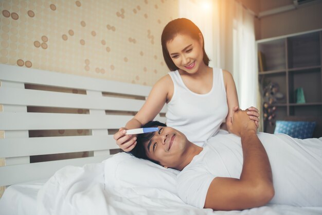 Pareja feliz sonriendo después de descubrir prueba de embarazo positiva en el dormitorio