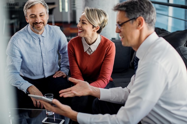 Pareja feliz y su agente de seguros usando tableta digital durante la reunión