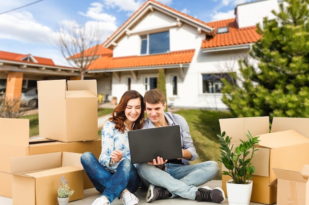 Pareja feliz con su nueva casa al fondo y sonriendo.